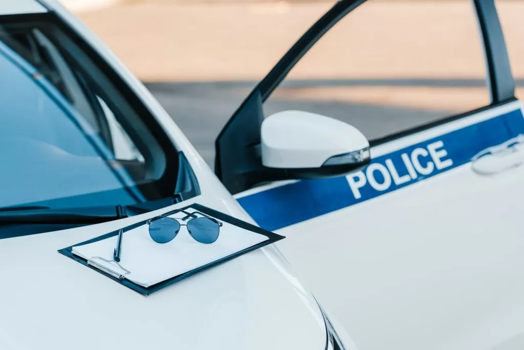 blank clipboard with sunglasses on automobile with flasher and lettering police at city street