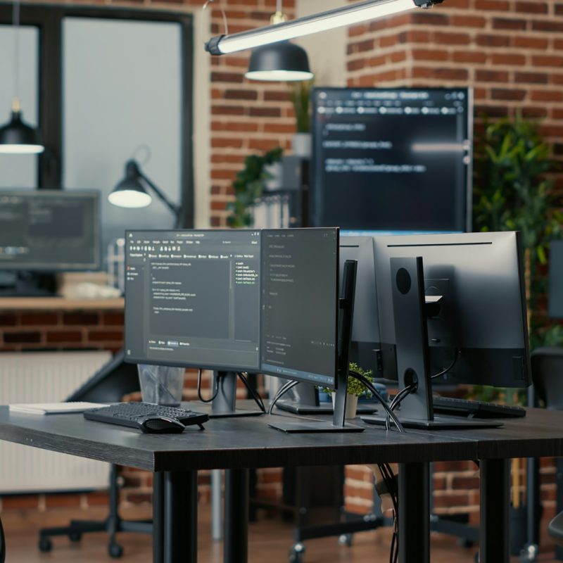 Computer screens running programming code in empty software developing agency office