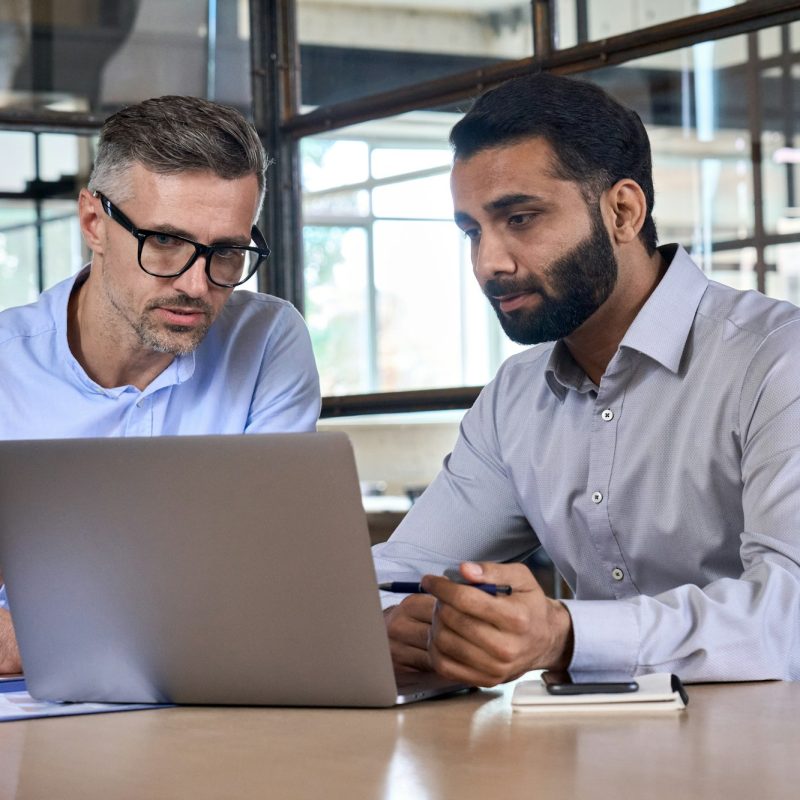 Two business men analysts discussing data management using laptop computer.