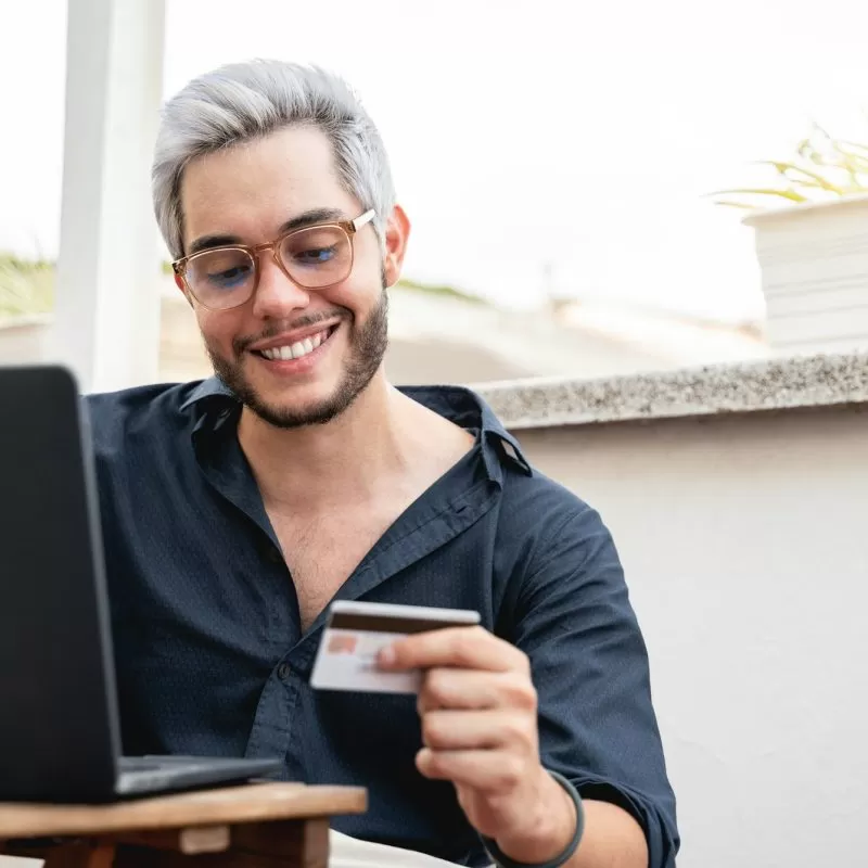 Young hipster man holding credit cart using computer laptop for online payment - E-commerce, bank